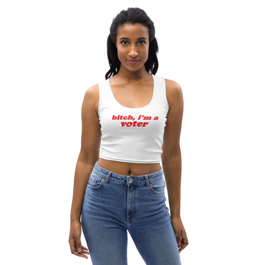 A woman wearing a white premium crop tank top featuring bold red retro typography that reads "bitch, i'm a voter".