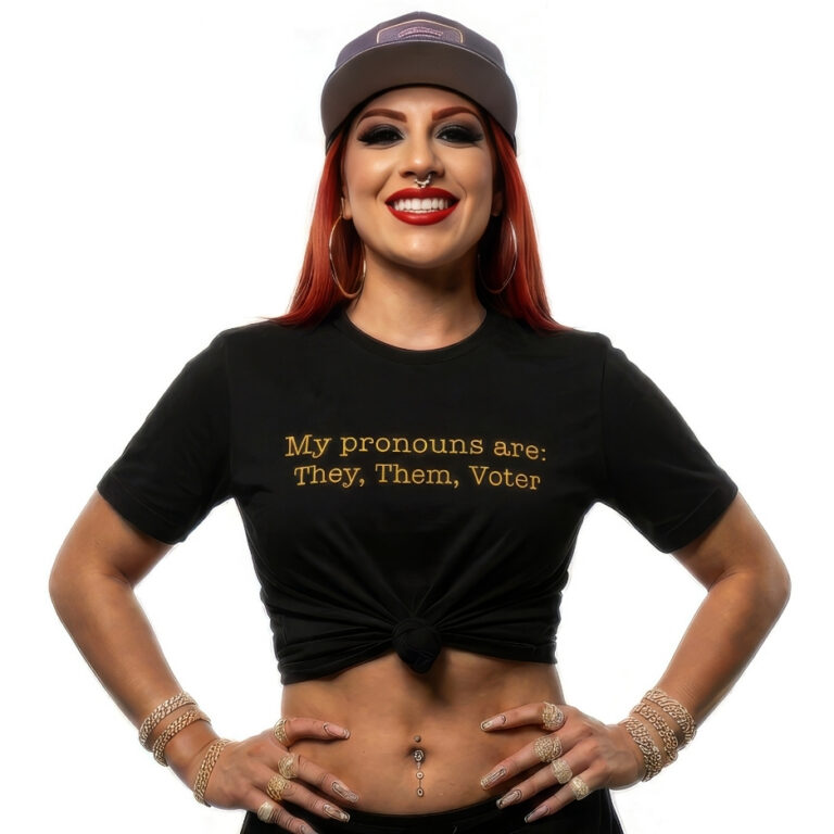 A confident person smiling 📸, wearing a black premium Bella+Canvas t-shirt with gold text reading My pronouns are: They, Them, Voter 🌟, promoting accessible voting.