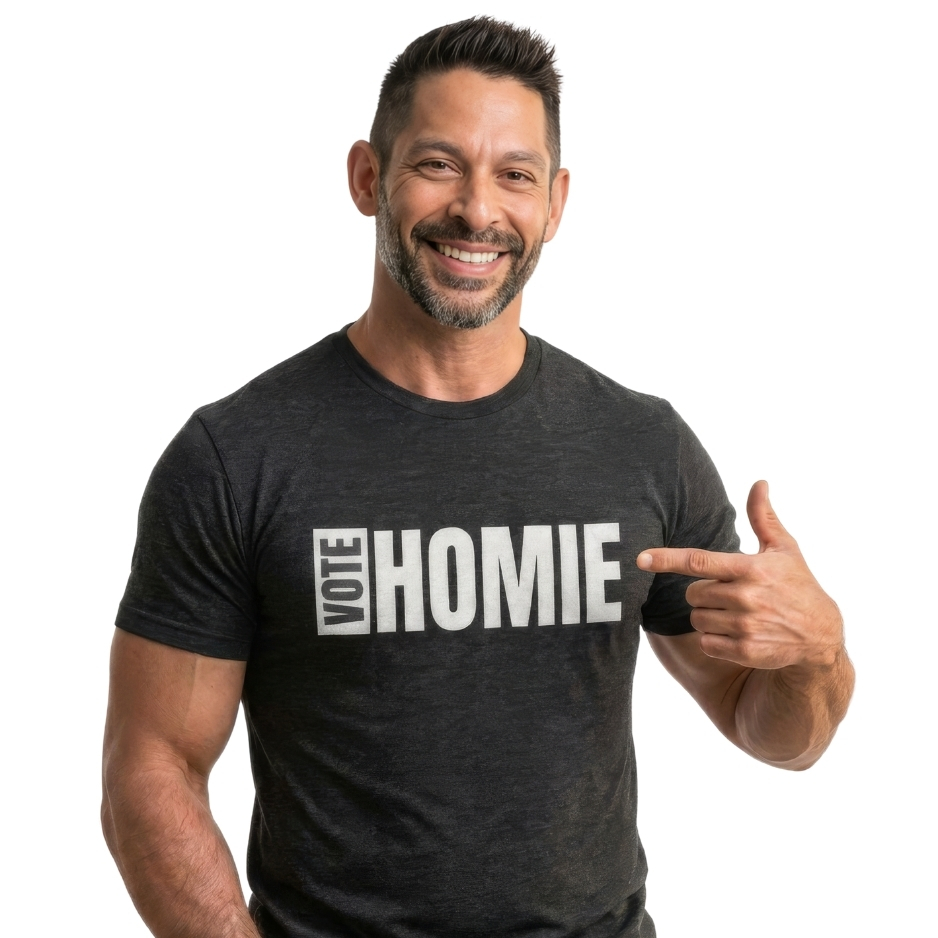 Jesse Alaniz, Executive Director of Protect November, smiling in a heather dark gray Vote Homie t-shirt pointing directly to the white block lettering on the chest against a white background.