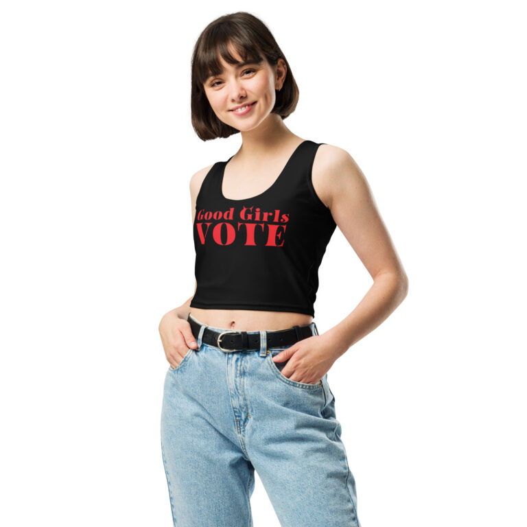 Young woman wearing a black crop tank with red Good Girls Vote stencil lettering and tiny devil horns, paired with high-waisted jeans