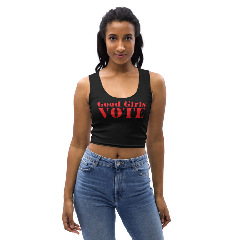 Young woman wearing a black crop tank with red Good Girls Vote stencil lettering and tiny devil horns, paired with high-waisted jeans